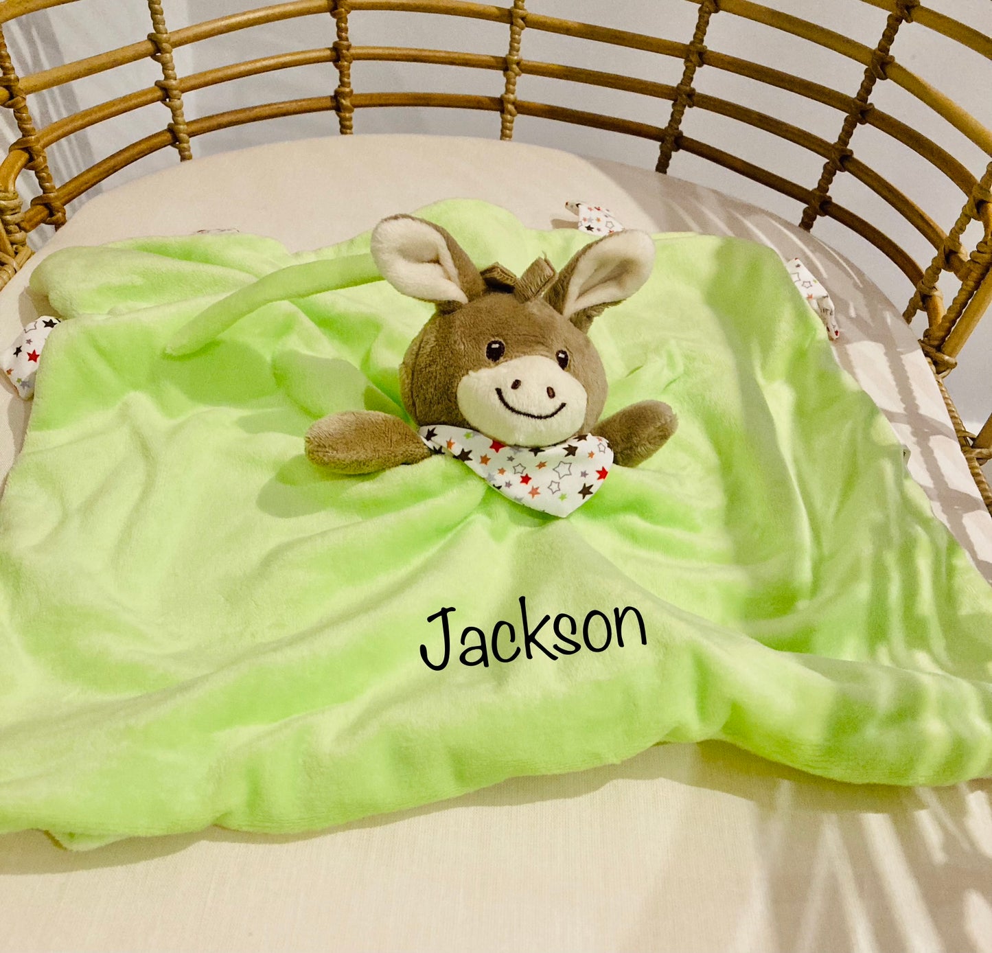Personalized green donkey baby comforter with the name 'Jackson' embroidered on it, displayed in a crib.