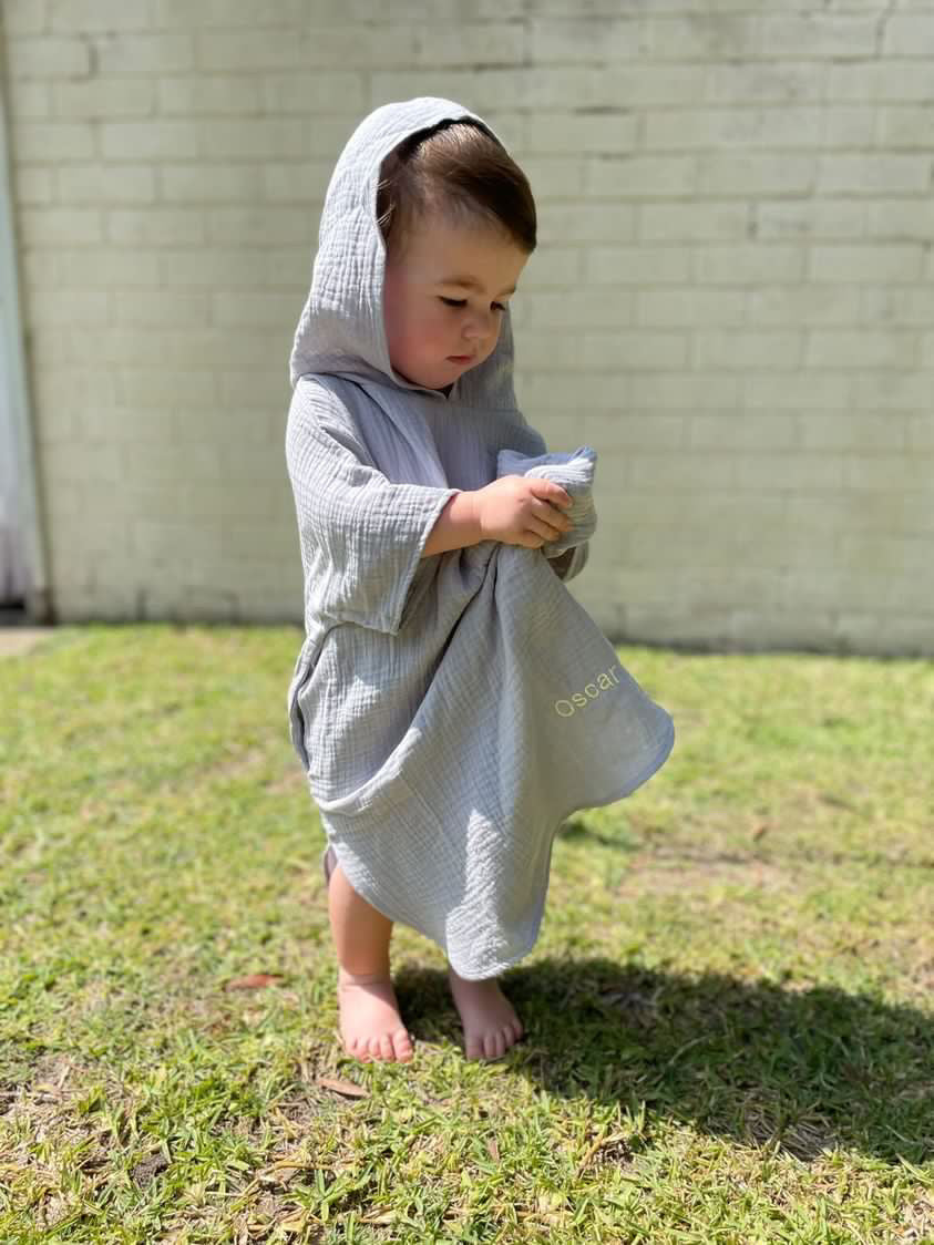 A boy wearing a muslin poncho outdoors with name 'Oscar'embroidered at the bottom of the poncho.
