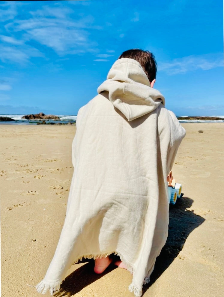 The back of the warm poncho warn by a child playing with a toy in the sand at the beach.