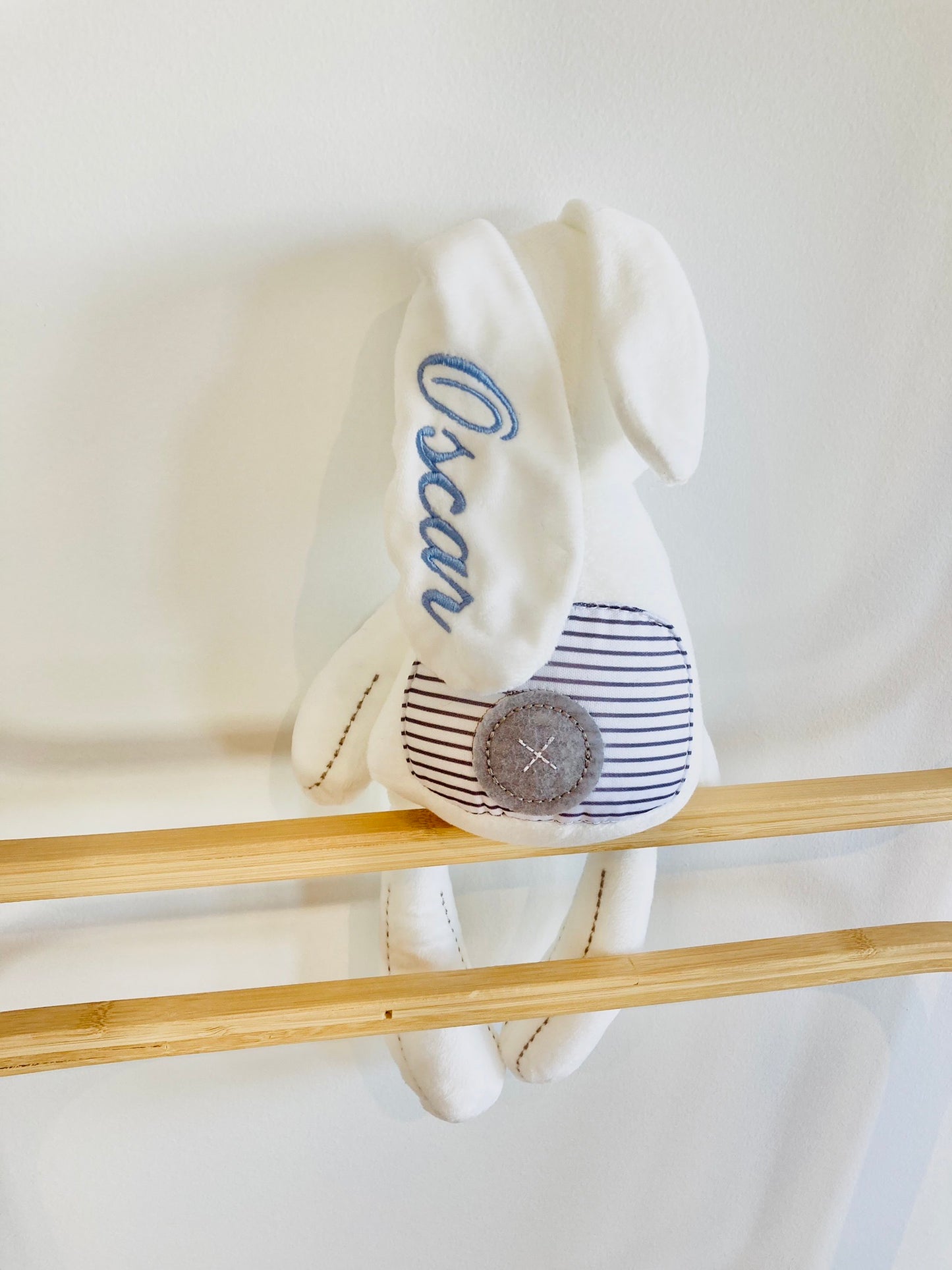 The back of the white bunny with an embroidered fabric button for the tail. Bunny ear is embroidered with 'Oscar'.