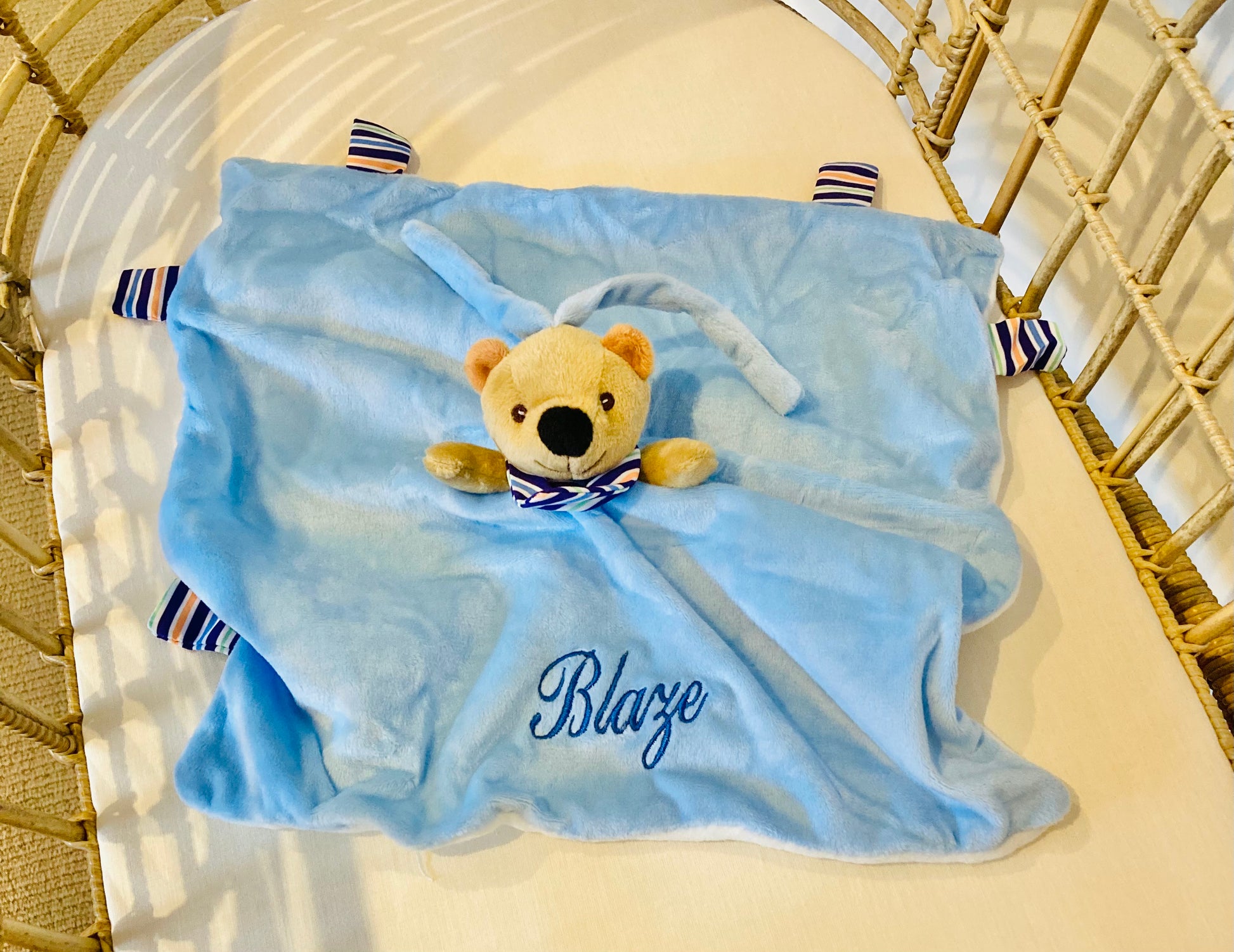 A blue Teddy Bear personalized baby comforter with striped side tabs, and embroidered name 'Blaze'.