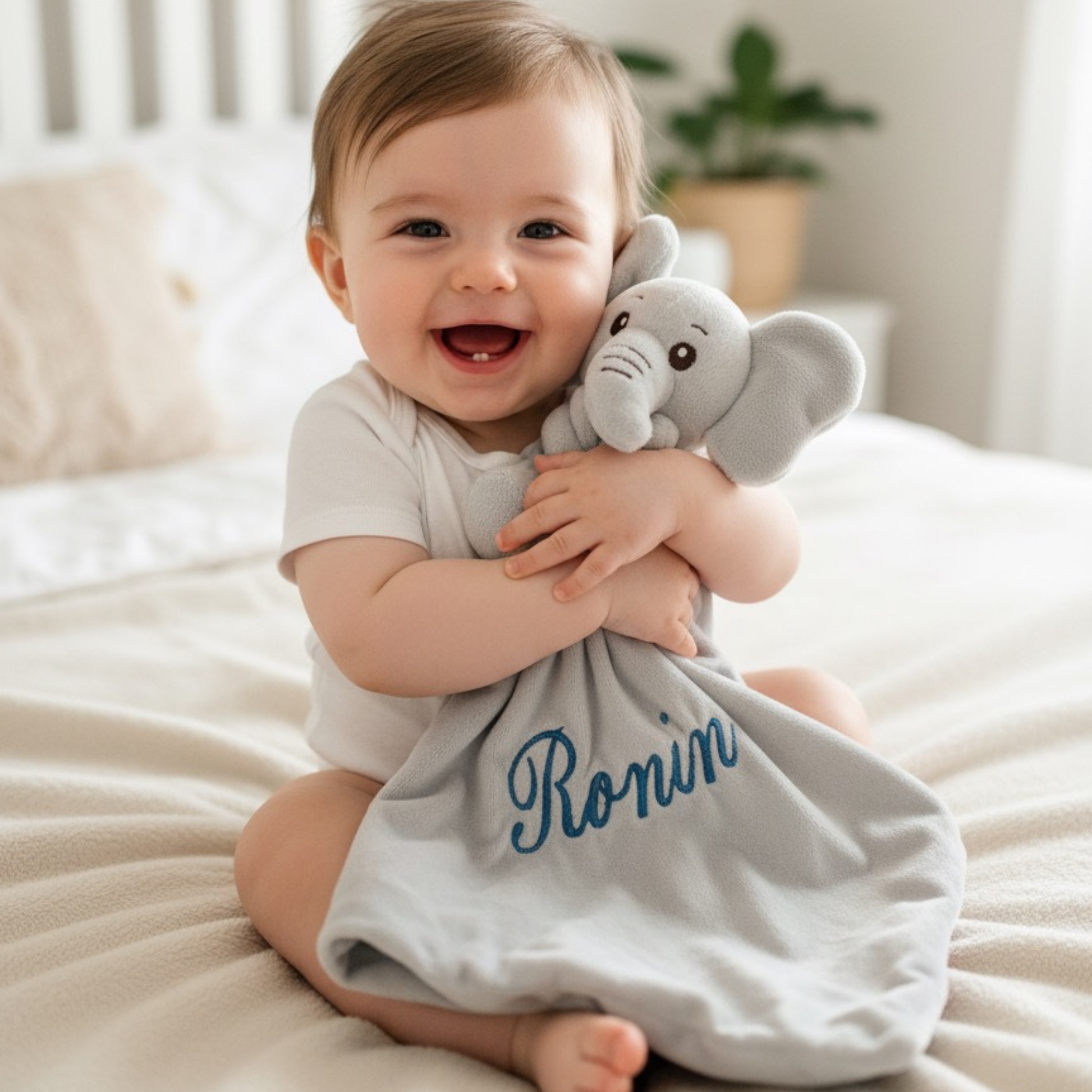 Baby holding a plush elephant baby comforter with 'Ronin' embroidered on a white blanket