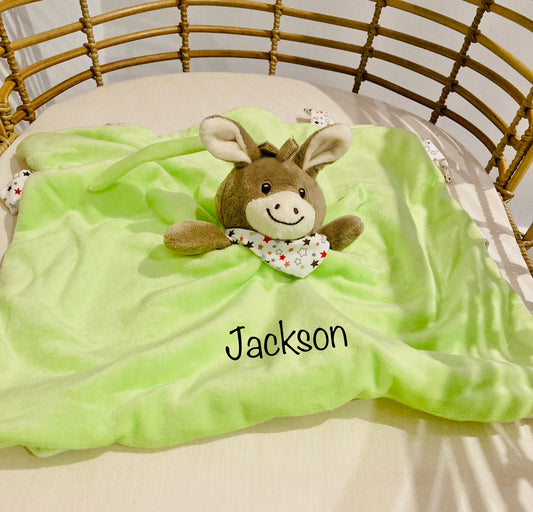Personalized green donkey baby comforter with the name 'Jackson' embroidered on it, displayed in a crib.