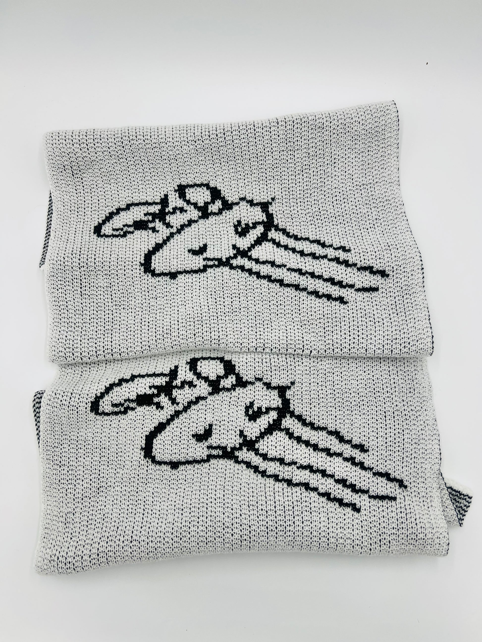Black and white knitted scarf folded showing repeated sections of kid drawing. 