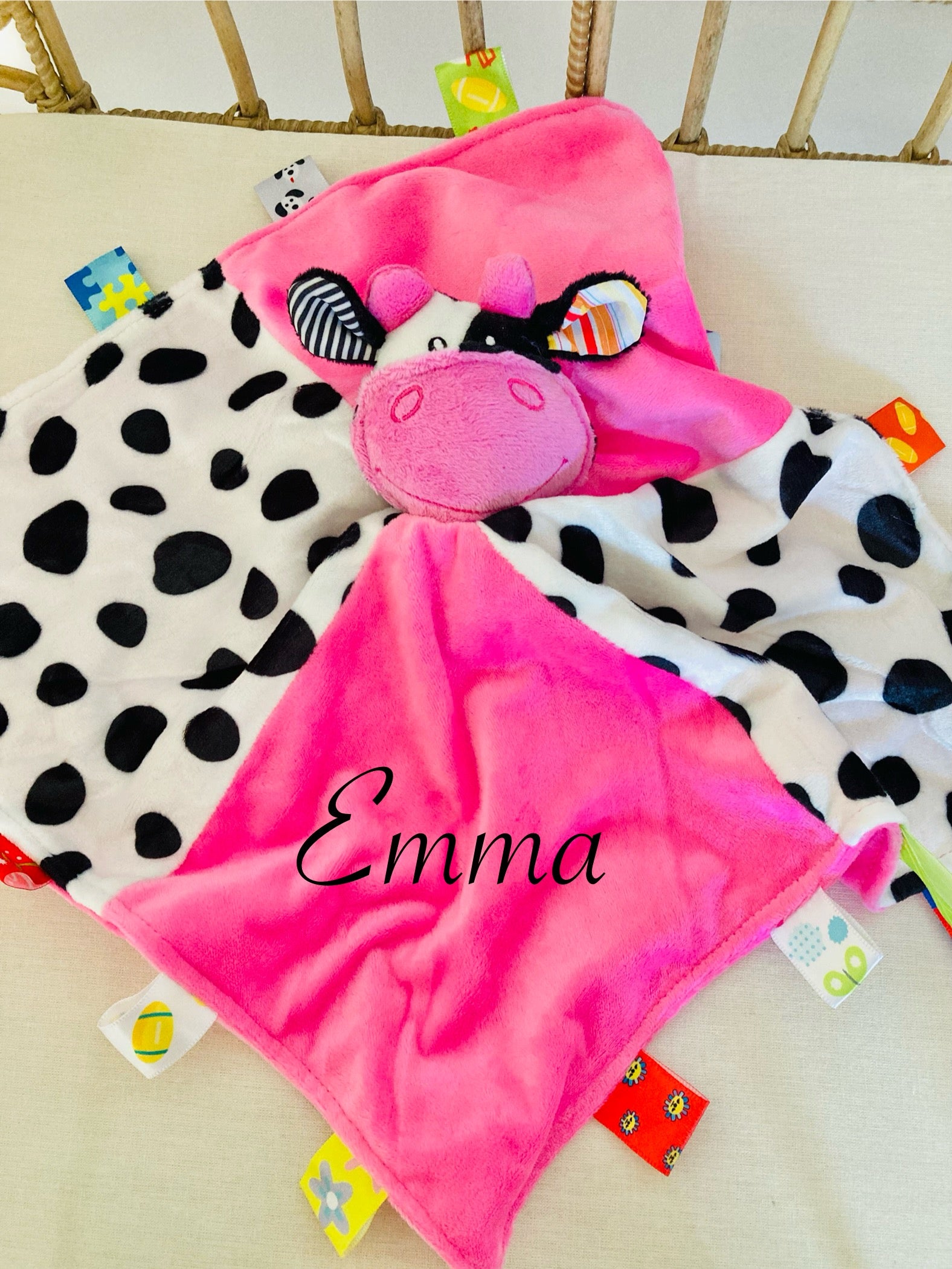Pink cow baby comforter in a cot. Baby comforter has four quarter sections, two in pink and two in cow print. The comforter has side tabs and a gentle rattle for sensory play. 
