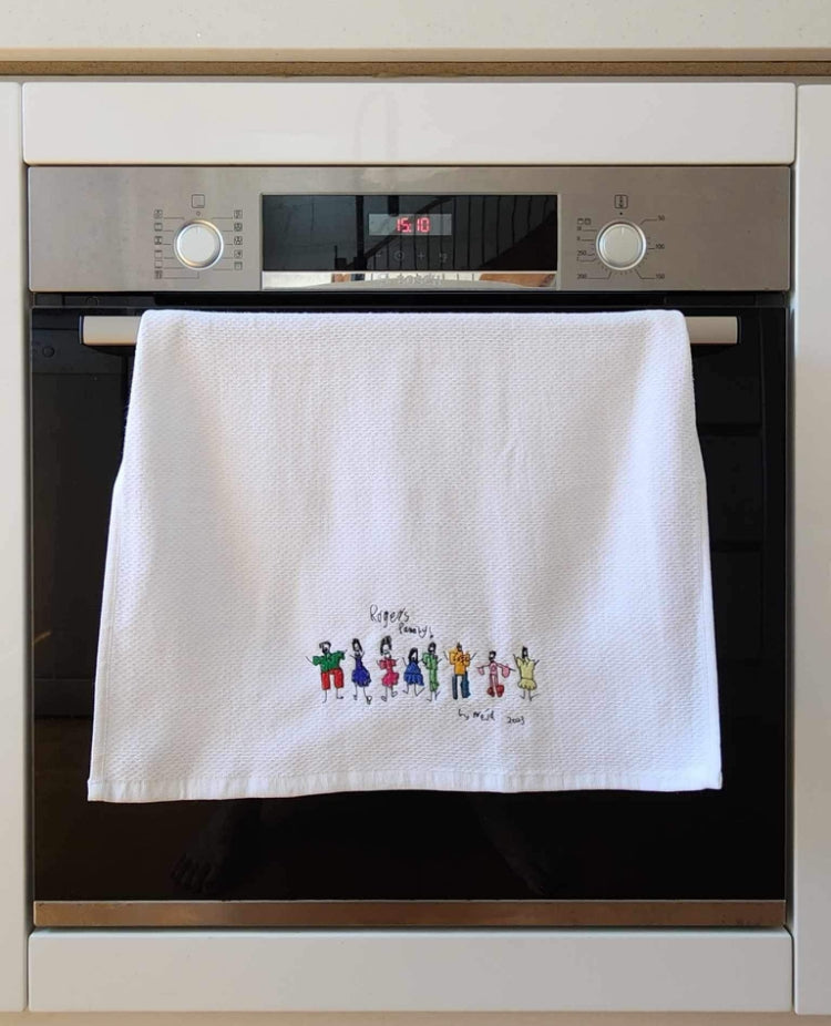 White towel with embroidered kid's drawing of family members, hanging on a modern oven.