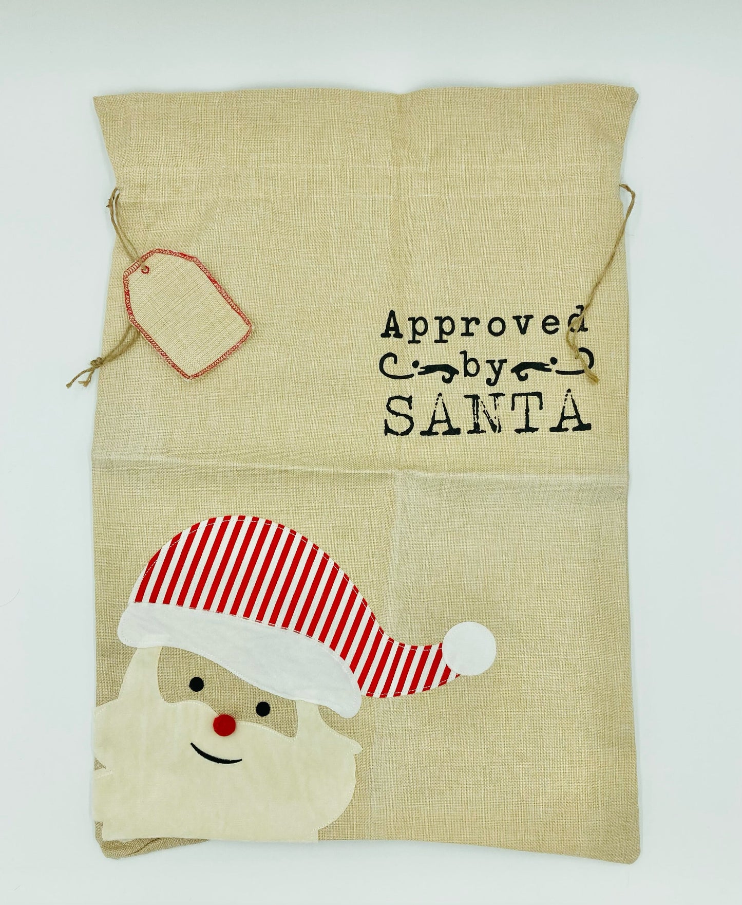 Santa sack with appliqued Santa and tag against a white background. Santa sack has printed words 'Approved by SANTA'. 